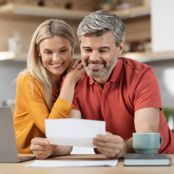 Paar im mittleren Alter sitz am Küchentisch und freuen sich über das positive Krebsscan Testergebnis, den sie in Papierform in der Hand halten